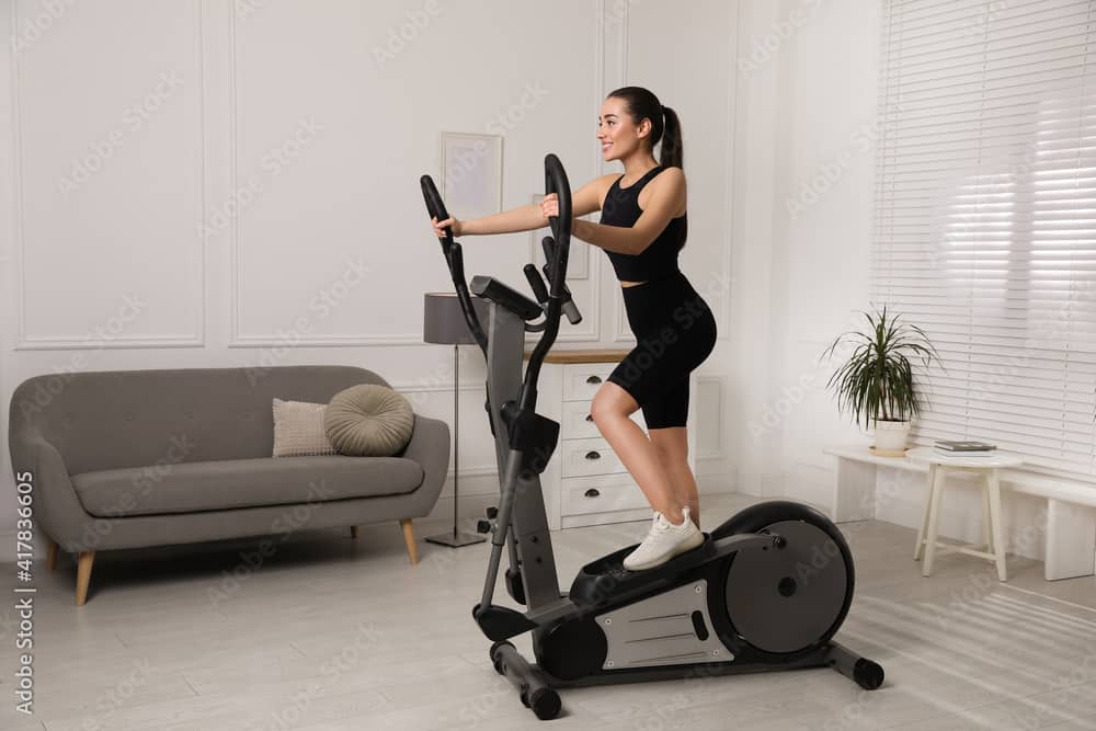 Happy young woman training on elliptical machine at home